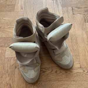 Beige Isabel Marant wedge sneakers - Chunky sneakers från Isabel Marant i beige mocka och skinn med coola paneler och dold kilklack. Snyggt vadderad design och kardborreband framtill. Perfekta för dig som vill ha streetstyle-vibe med extra höjd.