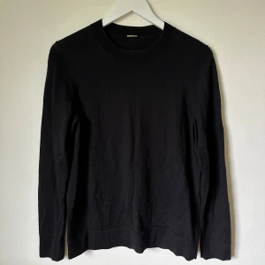 Svart stickad tröja från Arket - Svart stickad tröja från Arket i ekologisk ull. Klassisk rund hals och långärmad modell med ribbade muddar vid ärmslut och nederkant. Perfekt för lager-på-lager och enkel att matcha med jeans eller chinos. 1F8