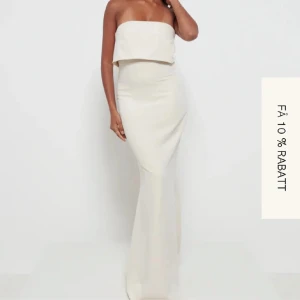 Vit axelbandslös långklänning - Elegant vit axelbandslös långklänning med en stilren design. Klänningen har en smickrande passform och en subtil slits baktill. Perfekt för balen.