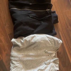 Svart och grå hoodie med dragkedja - Två hoodies med dragkedja, en svart från 157 i storlek M och en ljusgrå från NEU i storlek S. Båda har huva med snörning och är långärmade. Perfekt för chill dagar och streetstyle. Materialet känns som mjuk bomull och polyesterblandning.
