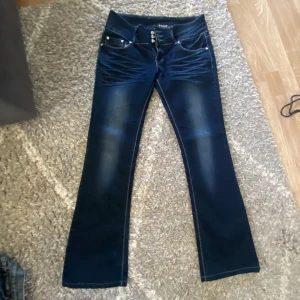 Lågmidjade utsvängda jeans  - Snygga mörkblå jeans från gouse med bootcut passform. Byxorna har dekorativa knappar, kontrastsömmar och broderade bakfickor. Materialet är stretchigt med 96% bomull och 4% elastan för extra komfort. Storlek W30💗jag uppfattar dom som små i storleken och skulle uppskatta till storlek s 