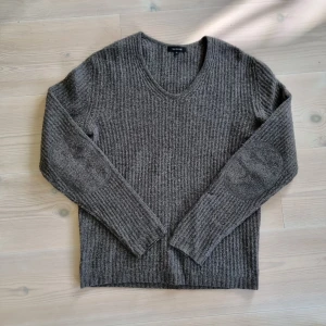 Grå stickad tröja från Paul & friend - Mysig grå stickad tröja från Paul & friend i storlek L. Tröjan har ribbad struktur, rund halsringning och förstärkta armbågslappar. Perfekt för kyliga dagar och enkel att matcha med jeans eller chinos.