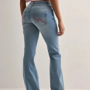 Ljusblå bootcut jeans med broderi - Säljer ett par ljusblå bootcut jeans från Nelly med rosa zigzag-brodering på bakfickorna. Jeansen har låg midja, klassisk femficksdesign. Finns en pytteliten blek fläck på ena låret som knappt märks av därav sänkt pris. Nypris 699kr. I övrigt super bra skick!