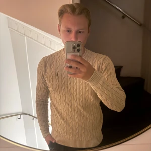 Beige kabelstickad tröja Polo Ralph Lauren - Säljer en beige kabelstickad tröja från Polo Ralph Lauren. Tröjan har rund halsringning, ribbade muddar och det klassiska broderade logotypen på bröstet. Perfekt för dig som gillar en clean och tidlös stil.
