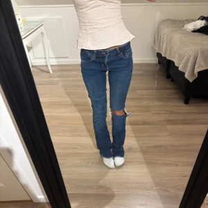 Blå bootcut jeans med slitning - Säljer ett par blå jeans med bootcut-modell och snygg slitning vid ena knät. Passar mig som är 160 cm