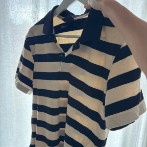 Randig pikétröja från H&M, svart/vit - Snygg pikétröja från H&M i relaxed fit med breda svarta och vita ränder. Klassisk krage och knäppning framtill, kortärmad och perfekt för en chill och stilren look. Passar dig som gillar enkel men trendig stil.