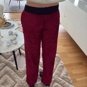 Vinröda mjukisbyxor med svart midja - Mysiga vinröda mjukisbyxor med bred svart resår i midjan. Byxorna har rak passform och är gjorda i ett mjukt, fluffigt material som känns riktigt skönt mot huden. Perfekta för chill dagar hemma eller när du vill vara extra bekväm.
