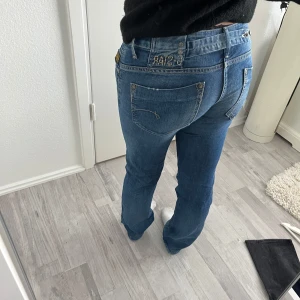 Blå jeans från G-Star RAW - Säljer ett par klassiska blå jeans från G-Star RAW med snygga detaljer och broderad logga bak. Jeansen har raka ben, normal passform. Innerbebslängd 82
