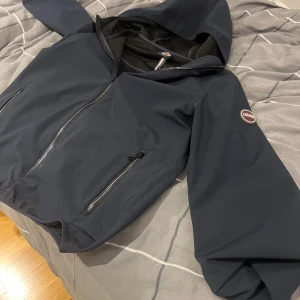 Mörkblå vindjacka från Colmar Ny pris cirka 3000 mitt pris 800 kr  - Säljer en stilren mörkblå vindjacka/Windbreaker från Colmar. Pga växt ur den. Jackan har en dragkedja framtill och två praktiska fickor med dragkedjor, även en gömd ficka inuti jackan. Den har en huva och ett diskret märke på ärmen. Perfekt för blåsiga dagar! 