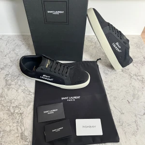 Svarta sneakers från Saint Laurent - Snygga svarta sneakers från Saint Laurent med vit sula och märkets logga på sidan. Skorna har snörning och är perfekta för en stilren look. Levereras med originalförpackning och dustbag.