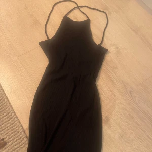 Svart ribbad klänning - Svart ribbad klänning med smala axelband och en figurnära passform. Midi lång. Ungefär ovanför knäskålarna på mig som är 175 cm. Öppen rygg med knyte bak. 