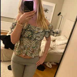 Mönstrad offshoulder blus - Säljer en färgglad offshoulder blus med volanger och blommigt mönster. Perfekt för sommardagar och ger en bohemisk känsla. Blusen har en lös passform och är lätt och luftig.