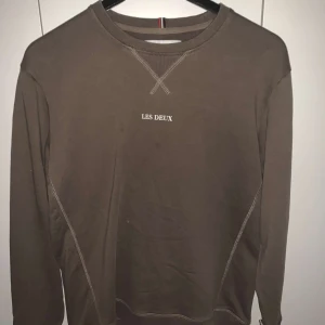 Brun tröja från Les Deux - Säljer en stilren brun tröja från Les Deux med rund halsringning och diskret logga på bröstet. Perfekt för en avslappnad look.