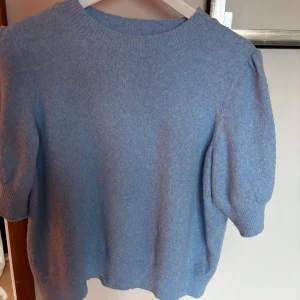 Blå tröja från Vero Moda - Säljer en ljusblå tröja från Vero Moda med korta ärmar och rund hals. Tröjan har en mjuk och bekväm känsla, perfekt för en avslappnad stil. Den är enkel och stilren, vilket gör den lätt att matcha med olika outfits.