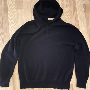 Svart kashmir hoodie från Sayles - Säljer en lyxig svart hoodie i mjuk kashmir från Sayles. Perfekt för kyliga dagar med sin bekväma passform och klassiska design. Den har en justerbar huva och långa ärmar. Ett måste för garderoben!