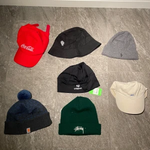Samling av olika huvudbonader - En samling av olika huvudbonader inklusive en röd Coca-Cola keps, en svart bucket hat, en grå stickad mössa, en blå mössa med tofs från Carhartt, en grön mössa från Stussy, en beige keps från och en svart mössa från Unisport. PM om ni vill köpa en eller flera. Pris diskuteras men billigt blir det! Stussy är såld. 