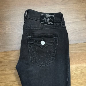 Gråa jeans från True Religion - Snygga gråa jeans från True Religion med låg midja och utsvängda ben. Modellen heter Joey low rise och är i storlek 27. Använd ett fåtal gånger(1 eller 2) så väldigt fint skick. Nypris 1299kr, säljes för 950 men pris kan diskuteras. 