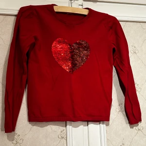 Röd tröja med paljett-hjärta från H&M - Säljer en röd tröja från H&M med ett stort paljett-hjärta på framsidan. Tröjan har långa ärmar och är perfekt för att lysa upp garderoben. Paljetterna ger en glittrig touch som gör den extra speciell. Perfekt för alla hjärtans dag eller när du vill sprida lite kärlek! ❤️