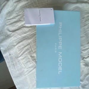  Philippe Model - Snygga vita sneakers från Philippe Model med bruna detaljer och snörning. Skorna har en klassisk design med en logotyp på sulan och en bekväm passform. Perfekta för en stilren look.