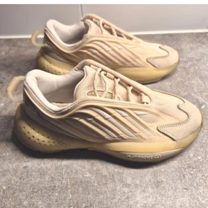 Beige sneakers från Adidas - Snygga beige sneakers från Adidas med en futuristisk design och mjuka linjer. Skorna har snörning och en unik sula som ger extra komfort. Perfekta för dig som vill ha en stilren look med en twist.