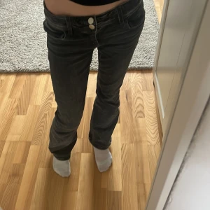 Svarta jeans från Gina Tricot - Snygga svarta jeans från Gina Tricot med låg midja och raka ben. De har en klassisk femficksdesign och stängs med två knappar framtill. Perfekta för en avslappnad stil.