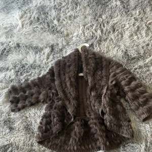 Brun pälsjacka från Derhy - Säljer en snygg brun pälsjacka från Derhy. Jackan har en fluffig och mjuk textur med trekvartsärmar och en öppen front. Perfekt för att hålla sig varm och stilren under kyliga dagar.