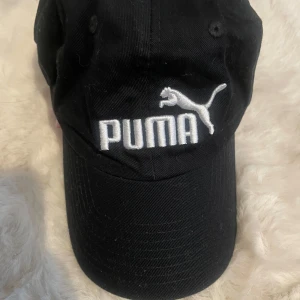 Svart keps från Puma - Snygg svart keps från Puma med broderad logga i vitt framtill. Perfekt för en sportig look eller som en stilren accessoar till vardagsoutfiten.