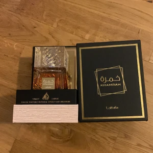 Khamrah Eau de Parfum från Lattafa - Exklusiv parfym från Lattafa, Khamrah, i en elegant flaska med en kristalliknande kork. Flaskan har en lyxig design med guldiga detaljer och rymmer 100 ml av doften. Perfekt för den som söker en unik och sofistikerad doftupplevelse.