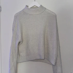 Beige stickad tröja från Kappahl - Säljer en mysig beige stickad tröja från Kappahl. Tröjan har en hög krage och långa ärmar, perfekt för kyliga dagar. Den ribbade strukturen ger en stilren look. Passar både till jeans och kjol!