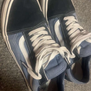 Svart och blå sneakers från Vans - Säljer ett par klassiska Vans sneakers i svart och blått med vita detaljer. Skorna har den ikoniska sidostripen och snörning framtill. Perfekta för en avslappnad stil.