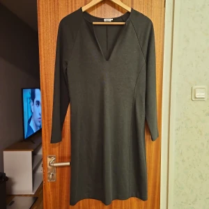 Mörkgrå klänning från Filippa K - Säljer en stilren mörkgrå klänning från Filippa K. Klänningen har en v-ringad design och långa ärmar, perfekt för en elegant look. Materialet är mjukt och bekvämt, vilket gör den idealisk för både vardag och speciella tillfällen.