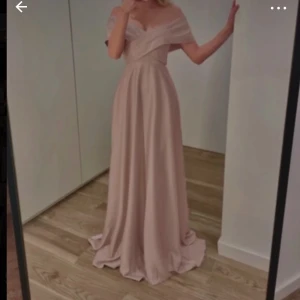 Champagnefärgad långklänning - Elegant champagnefärgad långklänning med offshoulder-design och omlott-detaljer. Perfekt för festliga tillfällen. Inte använd, perfekt för dig som är lång. 