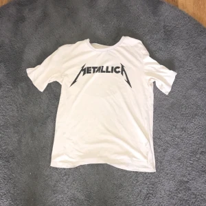 Beige Metallica t-shirt - Säljer en beige t-shirt med Metallica-logga i svart. Perfekt för fans av bandet! T-shirten har en klassisk passform och korta ärmar. 
