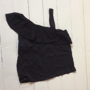 Svart oneshoulder topp från H&M - Snygg svart oneshoulder topp från H&M med volangdetalj. Perfekt för en stilren look. Tillverkad i ett mjukt material som ger en bekväm passform.