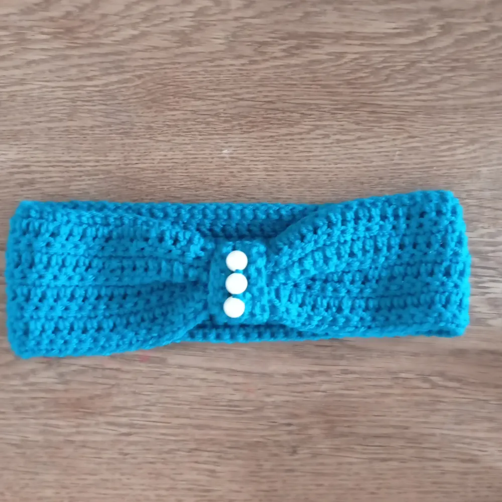 Snyggt mörkt turkost virkad pannband med tre vita pärlor framtill. Perfekt för att värma öronen med stil. Hemvirkad. Asusteet.