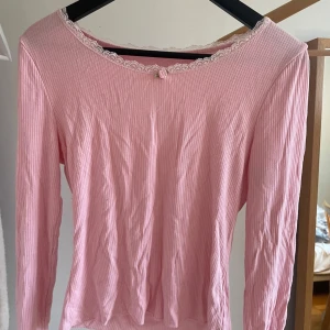 Rosa långärmad topp med spetsdetaljer - Söt rosa långärmad topp med ribbad struktur och spetsdetaljer vid halsringningen. Perfekt för en feminin och stilren look. Passar bra till både jeans och kjol.