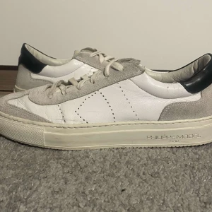 Phillipe model skor - Snygga vita sneakers från Philippe Model med grå mockadetaljer och svart häl. Skorna har en klassisk snörning och en stilren design som passar perfekt till vardags. Tillverkade i skinn och mocka för en lyxig känsla och skorna är i storlek 41. Hoppas du blir nöjd, Sbstyle :)