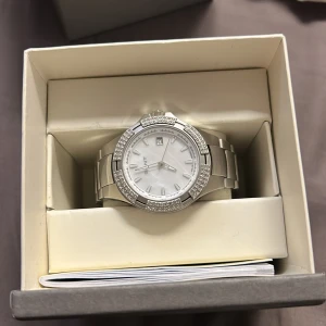 Silverfärgad klocka från GANT - Elegant silverfärgad klocka från GANT med en glittrig boett och vit urtavla. Klockan har en robust länkarmband i metall och levereras i originalförpackning. Perfekt för den som söker en stilren accessoar. Finns ej att köpa längre, nypris ca 2500kr