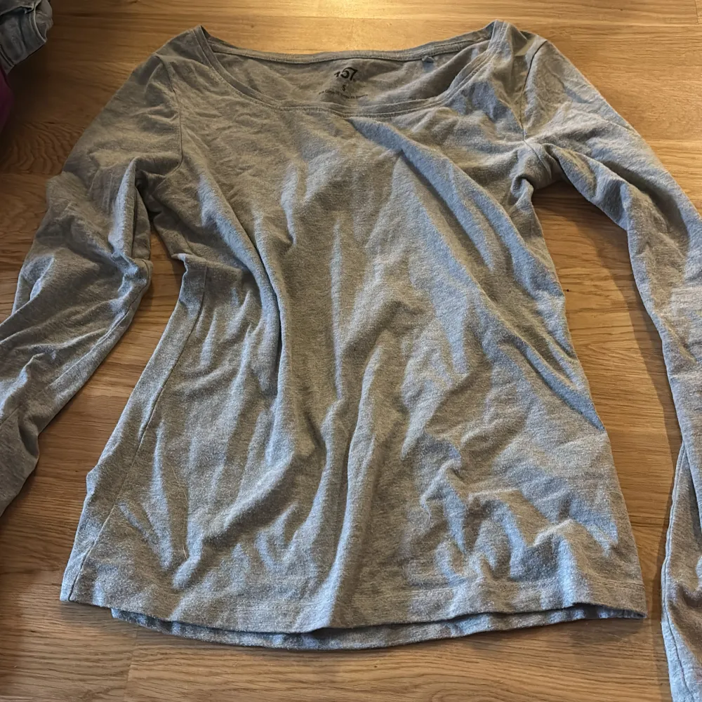Säljer en stilren grå långärmad topp med en bred halsringning. Perfekt för en avslappnad look. Passar bra till jeans eller kjol.. Neuletakit & Villapaidat.