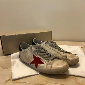 Golden goose skor - Snygga vita Golden goose skor med röd stjärna på sidan. Skorna har grå snörning och en svart häl. De är ganska använda och därav priset. Vid fler frågor eller bilder, kontakta.