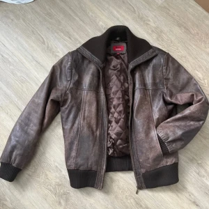 skinnjacka - Säljer en snygg brun skinnjacka med ribbade muddar och krage. Jackan har en dragkedja framtill och quiltat foder för extra komfort. Perfekt för höst och vår. Passar bra till både jeans och casual outfits. Liten fläck på höger arm, går nog att få bort men har själv inte orkat försöka lol