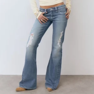 bootcut jeans med slitningar - Snygga blå bootcut jeans med slitningar på framsidan. Lågmidjade med dekorativa bakfickor med knappar. Oanvända med lapp kvar. Utsålda på Gina tricot.