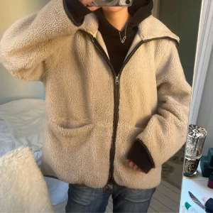 Beige teddyjacka med dragkedja - Mysig beige teddyjacka med dragkedja framtill. Jackan har en avslappnad passform och långa ärmar. Perfekt för kyliga dagar.