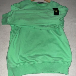 Grön tröja från Stone Island Junior || 11-12 - Snygg grön tröja från Stone Island Junior med rund hals och långärmade ärmar. Tröjan har en ikonisk logga på ärmen och är perfekt för en stilren look. Passar bra till både jeans och chinos.