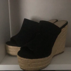 Svarta kilklackar från Marypaz - Snygga svarta kilklackar från Marypaz med öppen tå och hög flätad sula i naturmaterial. Perfekta för sommarens alla tillfällen.