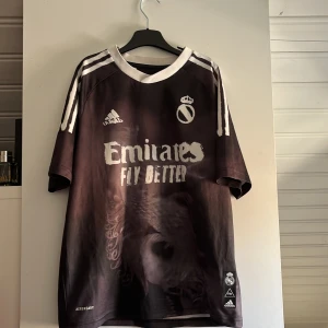 Real Madrid X Humanrace Limited edition shirt  - Säljer denna exklusiva Real Madrid X Humanrace tröja. En upplaga som inte säljs längre. Väldigt stilren men också en otroligt snygg och unik design. I princip aldrig använd då den endast har hängt uppe på en galge under flera års tid. Retailpris drygt 1000- 1500 kr. Mitt pris 750kr inkl frakt. Passar folk med storlek sen S och dels unisex 13-14 år. Då denna tröja är stor i storleken. Bara höra av sig vid frågor, hare gött!!
