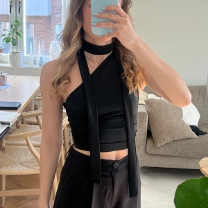 One shoulder topp med halsduk - Topp one shoulder med halsduk. Toppen är ärmlös och har en tight passform som framhäver figuren. Perfekt för en stilren och modern look.