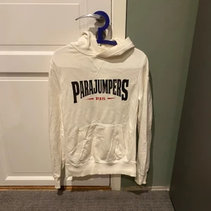 Vit hoodie från Parajumpers - Säljer en vit hoodie från Parajumpers med stor logga på framsidan. Tröjan har en klassisk känguruficka och är tillverkad i mjukt fleecematerial. Perfekt för kyliga dagar! Tröjan är använd fåtal gånger och är sparsamt använd