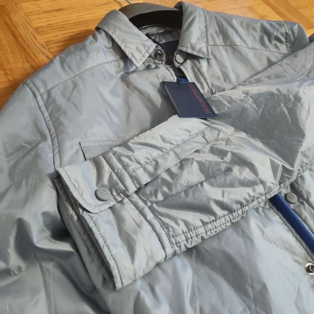 Säljer en helt ny jacka från Trussardi i storlek M med taggarna kvar, vilket gör den till ett utmärkt val för den som vill ha något fräscht och nytt. Denna stiliga jacka har en grå färg som ändras till en ljusgrön nyans beroende på ljuset. Den passar perfekt för både vardagliga och mer formella tillfällen, och kan enkelt stylas med alla sorts byxor. Tveka inte att kontakta mig för mer information. PRIS KAN DISKUTERAS!. Takit.