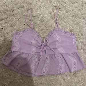 Lila spetsprydd linnetopp från FBSister - Söt lila linnetopp från Sister med spetsdetaljer och knytning framtill. Toppen har smala reglerbara axelband och en volangkant nedtill som ger en romantisk känsla. Perfekt för varma dagar eller sommarens fester.